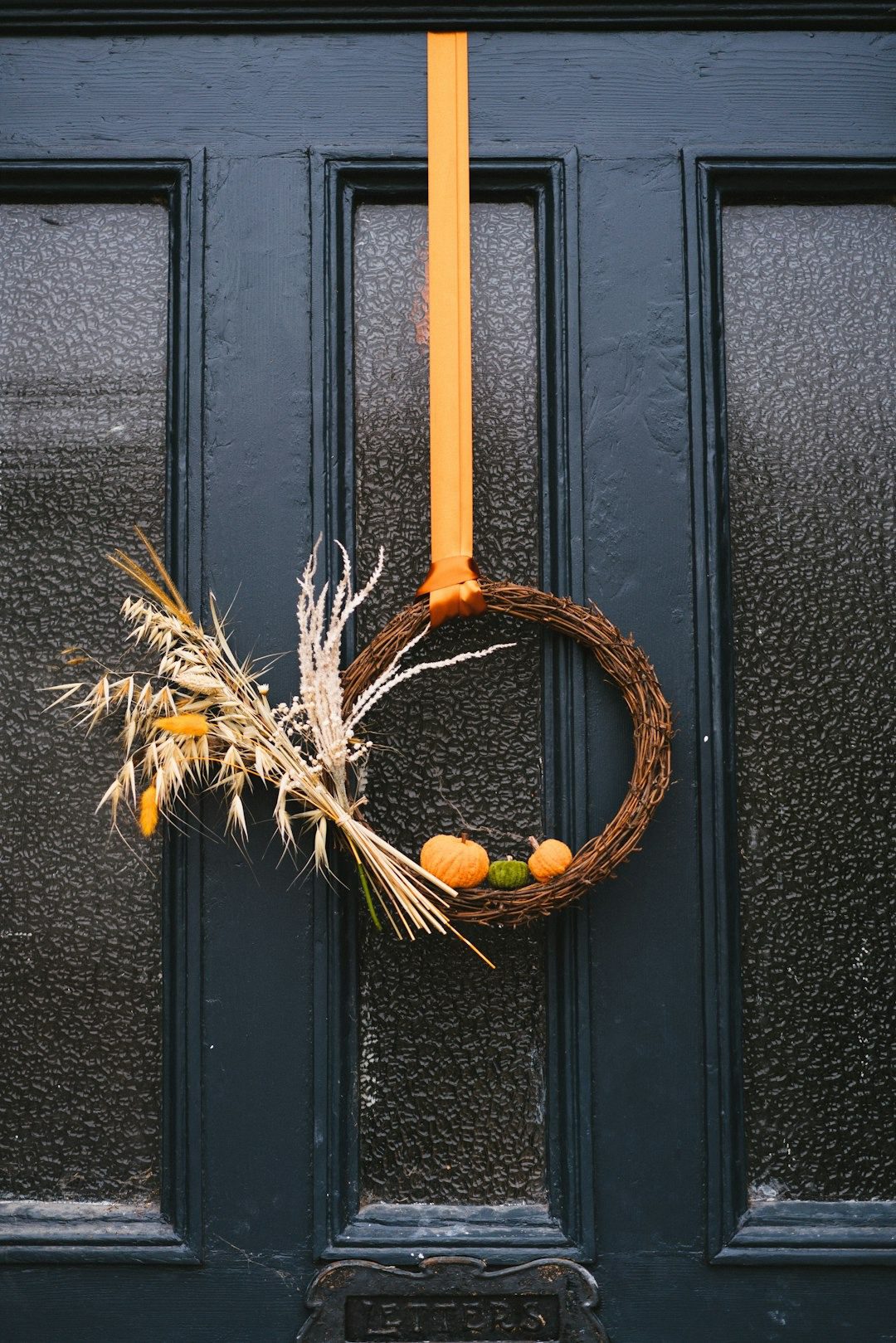 Mini pumpkin and autumn leaf wreath on a blue front door